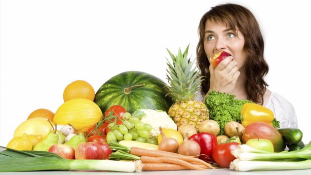 Woman eating an apple with a table full of produce before her.